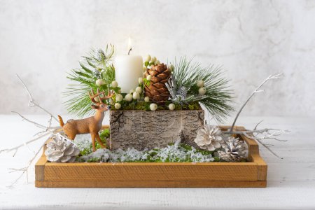 Photo for Christmas composition of candle,deer, pine cones, fir branches, flowers, moss, winter berries in wooden box. Cozy home winter concept. - Royalty Free Image