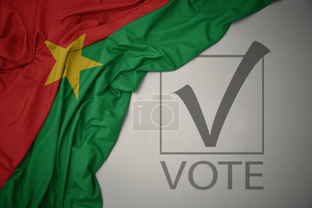 Foto de Ondeando colorida bandera nacional de Burkina faso sobre un fondo gris con voto de texto. concepto de elección. Ilustración 3D - Imagen libre de derechos