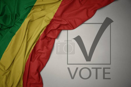 Foto de Ondeando colorida bandera nacional de la república del congo sobre un fondo gris con voto de texto. concepto de elección. Ilustración 3D - Imagen libre de derechos