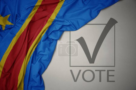Foto de Ondeando colorida bandera nacional de la república democrática del congo sobre un fondo gris con voto de texto. concepto de elección. Ilustración 3D - Imagen libre de derechos