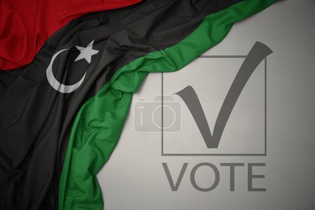 Foto de Ondeando colorida bandera nacional de la libya sobre un fondo gris con voto de texto. concepto de elección. Ilustración 3D - Imagen libre de derechos