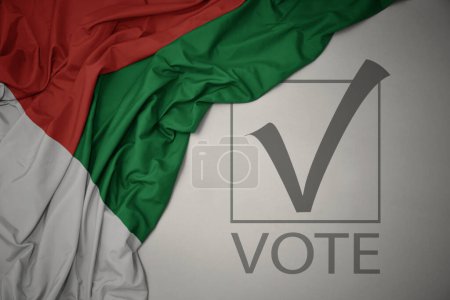 Foto de Ondeando colorida bandera nacional de madagascar sobre un fondo gris con voto de texto. concepto de elección. Ilustración 3D - Imagen libre de derechos