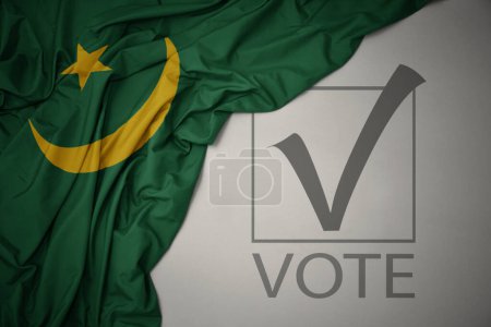 Foto de Ondeando colorida bandera nacional de Mauritania sobre un fondo gris con voto de texto. concepto de elección. Ilustración 3D - Imagen libre de derechos