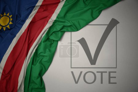 Foto de Ondeando colorida bandera nacional de namibia sobre un fondo gris con voto de texto. concepto de elección. Ilustración 3D - Imagen libre de derechos