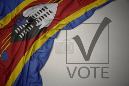 Foto de Ondeando colorida bandera nacional de eswatini sobre un fondo gris con voto de texto. concepto de elección. Ilustración 3D - Imagen libre de derechos