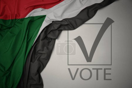 Foto de Ondeando colorida bandera nacional de sudan sobre un fondo gris con voto de texto. concepto de elección. Ilustración 3D - Imagen libre de derechos