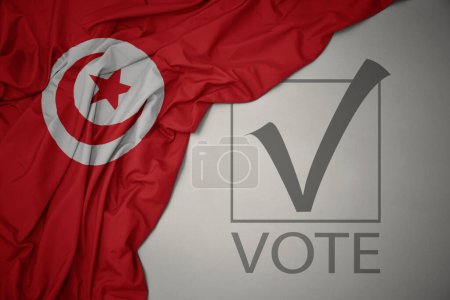 Foto de Ondeando colorida bandera nacional de Tunisia sobre un fondo gris con voto de texto. concepto de elección. Ilustración 3D - Imagen libre de derechos