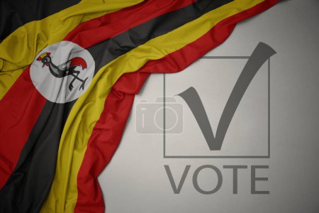Foto de Ondeando colorida bandera nacional de uganda sobre un fondo gris con voto de texto. concepto de elección. Ilustración 3D - Imagen libre de derechos
