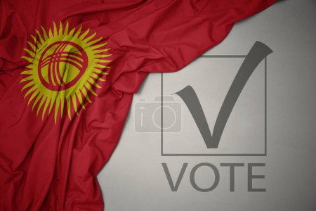 Foto de Ondeando colorida bandera nacional de Kirguistán sobre un fondo gris con voto de texto. concepto de elección. Ilustración 3D - Imagen libre de derechos