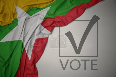 Foto de Ondeando colorida bandera nacional de myanmar sobre un fondo gris con voto de texto. concepto de elección. Ilustración 3D - Imagen libre de derechos