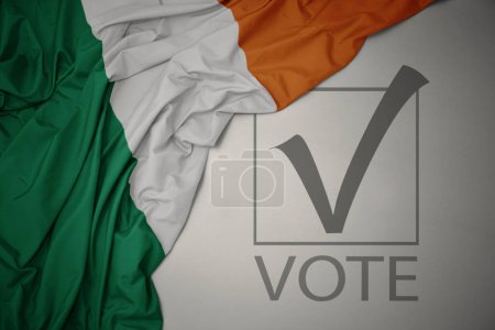 Foto de Ondeando colorida bandera nacional de Irlanda sobre un fondo gris con voto de texto. concepto de elección. Ilustración 3D - Imagen libre de derechos