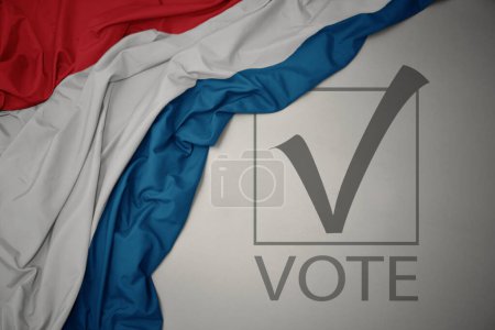 Foto de Ondeando colorida bandera nacional de Luxemburgo sobre un fondo gris con voto de texto. concepto de elección. Ilustración 3D - Imagen libre de derechos