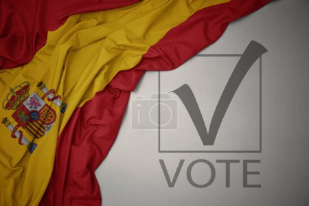 Foto de Ondeando colorida bandera nacional de España sobre un fondo gris con voto de texto. concepto de elección. Ilustración 3D - Imagen libre de derechos