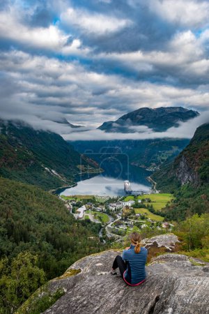Téléchargez les photos : Touriste en Norvège - Femme admire la vue du point pittoresque sur une colline, bateau de croisière le long de Geiranger & Geirangerfjorden. - en image libre de droit