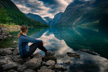 Téléchargez les photos : Touriste admire Lovatnet lac Norvège fjord norvégien serein avec des eaux cristallines entourées de montagnes imposantes - en image libre de droit