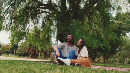 Photo for Happy smiling couple talking while sitting on blanket in park - Royalty Free Image