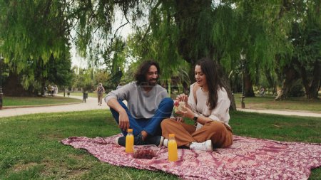 Photo for Laughing couple enjoying drinks at picnic in the park - Royalty Free Image