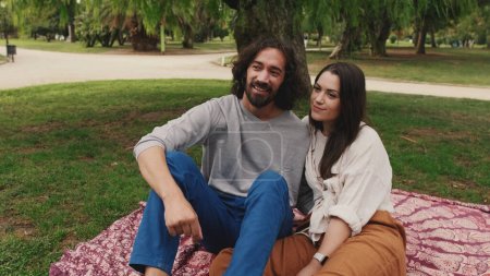 Glücklich lächelndes Paar im Gespräch, während es auf einer Decke im Park sitzt. Nahaufnahme