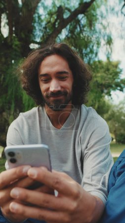 Photo for Young man using mobile phone while sitting on the lawn in the park - Royalty Free Image