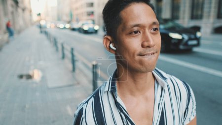Young man walks next to the road and listens to music with headphones