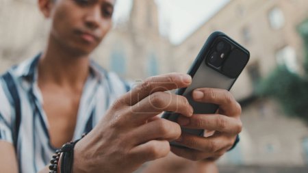 Junger Mann Tourist auf Stufen benutzt Handy, während er auf Wahrzeichen sitzt Hintergrund