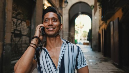 Photo for Young man tourist walks along narrow street of the old city and talks on mobile phone - Royalty Free Image