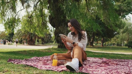 Photo for Young woman using phone in the park - Royalty Free Image