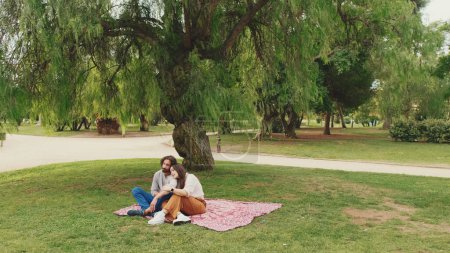 Photo for Happy smiling couple talking while sitting on blanket in park - Royalty Free Image
