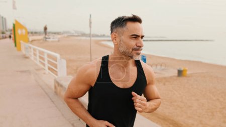 Homme musclé d'âge moyen court le long de la promenade avant de faire du jogging