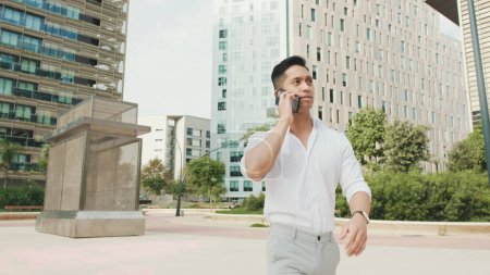 Photo for Young businessman talking on smartphone on modern buildings background - Royalty Free Image