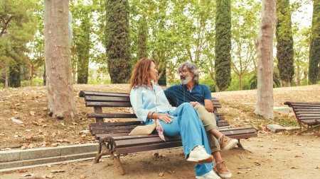Photo for Happy couple talking while sitting on bench outside in the park in autumn - Royalty Free Image