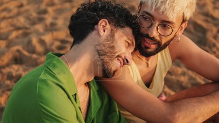 Téléchargez les photos : Moments romantiques, couple homosexuel jouissant de rapports sexuels les uns avec les autres tout en étant assis sur la plage à l'aube - en image libre de droit