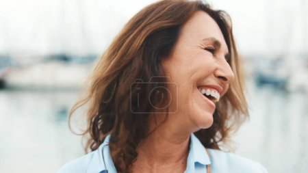 Close up, happy attractive middle age woman standing in port on yacht background looking at camera with smile