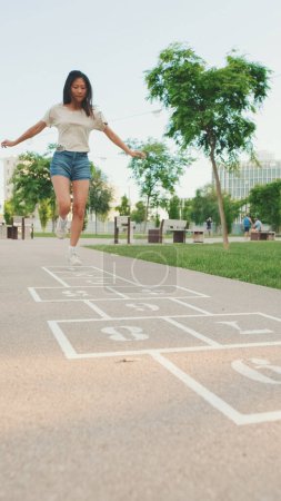 Photo for Joyful beautiful brunette girl dressed in casual clothes playing hopscotch game outdoors, having fun - Royalty Free Image
