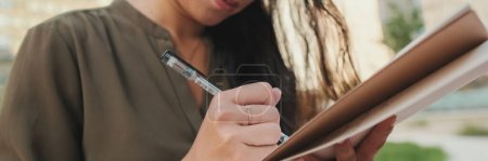 Photo for Young girl looks through notes in notebook while sitting on modern buildings background, Close up, Panorama - Royalty Free Image