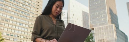 Photo for Young girl uses laptop pc outside on modern buildings background, Panorama - Royalty Free Image