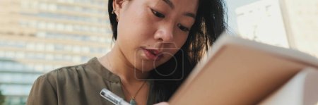 Photo for Young girl looks through notes in notebook while sitting on modern buildings background, Close up, Panorama - Royalty Free Image