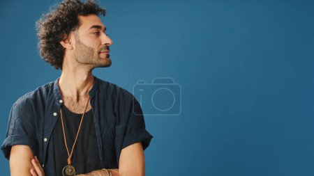 Mann mit lockigem Haar, in blauem Hemd gekleidet, schaut zur Seite, um Platz für Werbung auf blauem Hintergrund im Studio zu zeigen