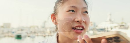 Photo for Close up, young woman talking on speakerphone mobile phone on seascape background, Panorama - Royalty Free Image