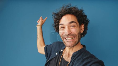 Lächelnder Mann mit lockigem Haar, blaues Hemd, Blick in die Kamera, Videoanruf, Willkommensschild isoliert auf blauem Hintergrund im Studio