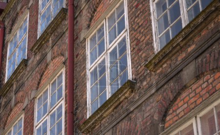 Foto de Viejas ventanas de madera en la fachada de un antiguo edificio de ladrillo con una tubería de agua - Imagen libre de derechos