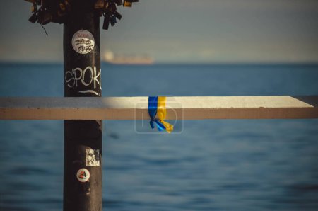 Foto de Cintas azules y amarillas están atadas a la barandilla metálica de un muelle en la orilla del mar junto a un poste de luz - Imagen libre de derechos