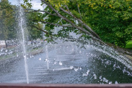 Foto de Salpicaduras de una fuente volando a través de un río o canal contra un fondo de árboles verdes en un parque de la ciudad - Imagen libre de derechos