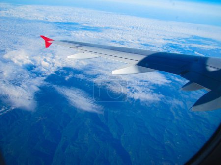 Foto de Vista de nubes y montañas en la superficie de la tierra bajo el ala de un avión desde abajo desde la ventana del avión - Imagen libre de derechos