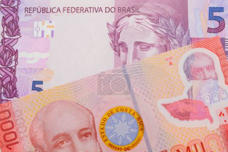 Foto de Una imagen macro de un billete de cinco reales rosa y púrpura de Brasil emparejado con un colorido billete rojo de mil colones de Costa Rica. Disparo de cerca en macro. - Imagen libre de derechos