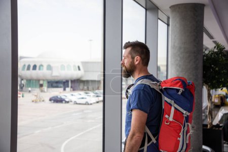 Foto de Hombre guapo con mochila esperando en el aeropuerto - Imagen libre de derechos