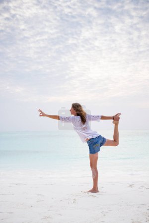 Téléchargez les photos : Femme faisant du yoga par la mer couleurs pastel - en image libre de droit