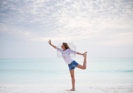 Téléchargez les photos : Femme faisant du yoga par la mer couleurs pastel - en image libre de droit