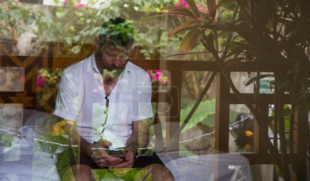 Foto de Hombre guapo mirando a través de la ventana que refleja las plantas tropicales salud mental - Imagen libre de derechos