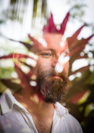 Foto de Hombre guapo mirando a través de la ventana que refleja las plantas tropicales salud mental - Imagen libre de derechos